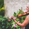 Side view of Maura playing the violin beside flowers