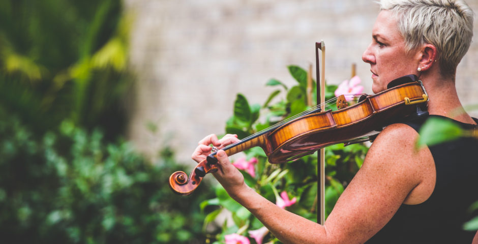Side view of Maura playing the violin beside flowers